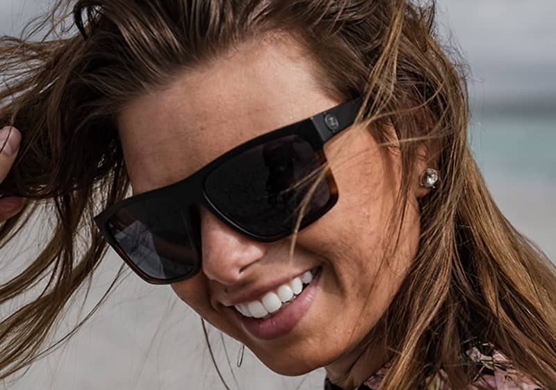 Žena s dlhými vlasmi v okuliaroch na pláži.