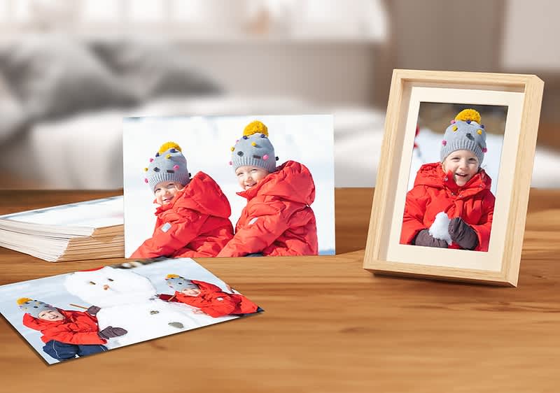 Dieťa v červenej bunde s čiapkou, snehuliak, fotografie na drevenom stole