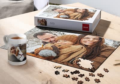 Puzzle s rodinnou fotografiou na stole, vedľa šálka s fotkou ženy a krabica puzzle