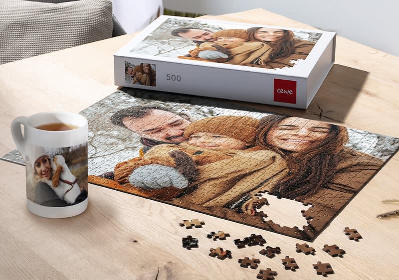 Puzzle s rodinnou fotografiou na stole, vedľa šálka s fotkou ženy a krabica puzzle