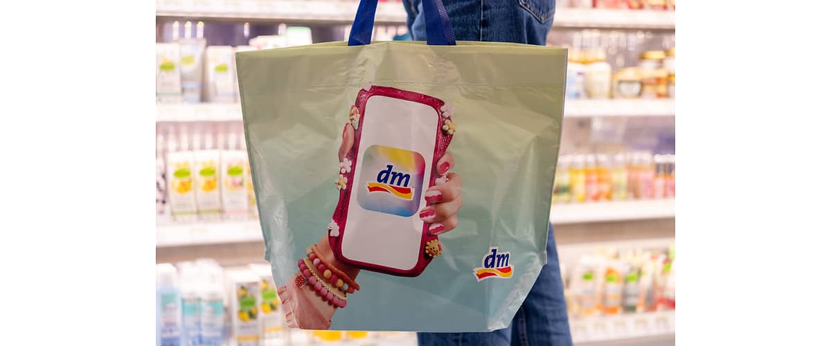 Nákupná taška s logom dm zobrazujúcim telefón a rukou s náramkami