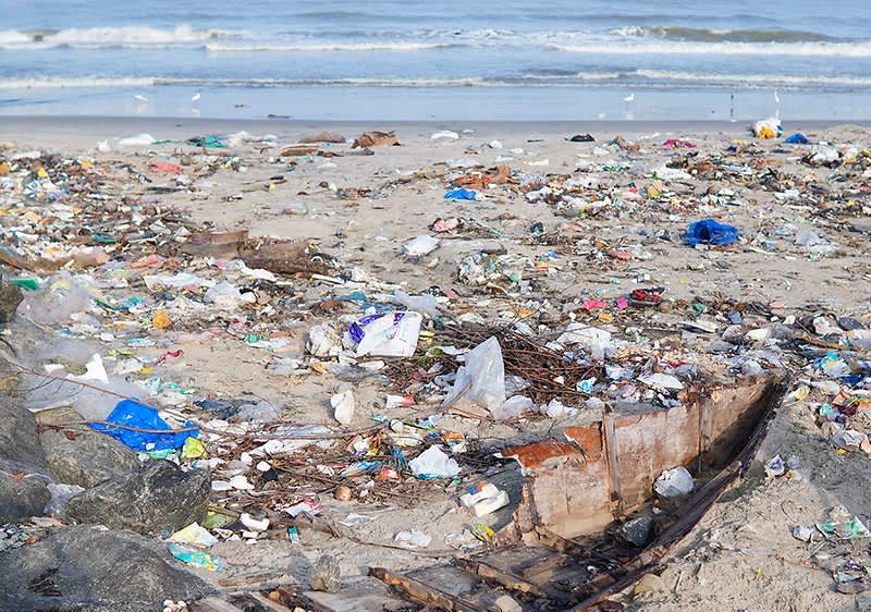 Onesnažena plaža z odpadki in valovi v ozadju
