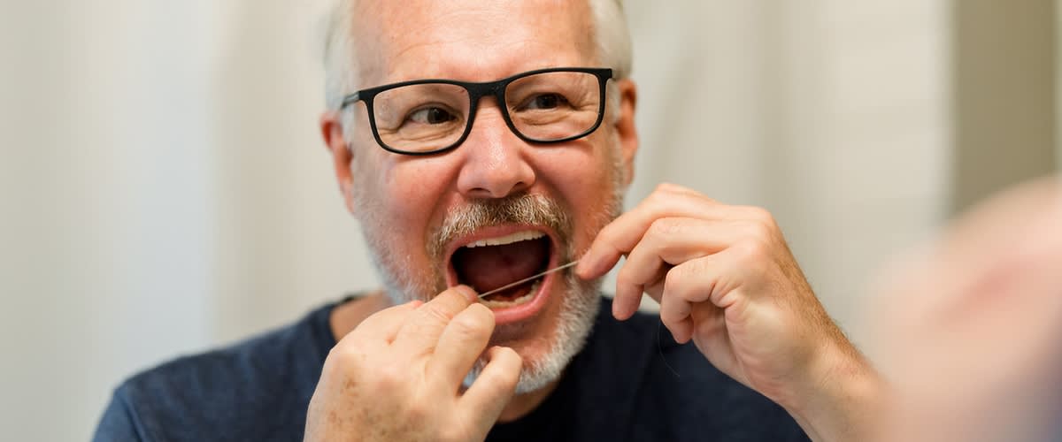 Oseba si z zobno nitko čisti zobe