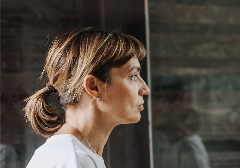 Oseba z rjavimi lasmi v čopu, oblečena v belo majico