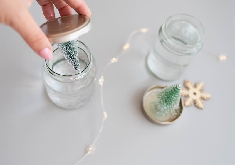 Oseba odpira kozarec z majhno božično drevesce.