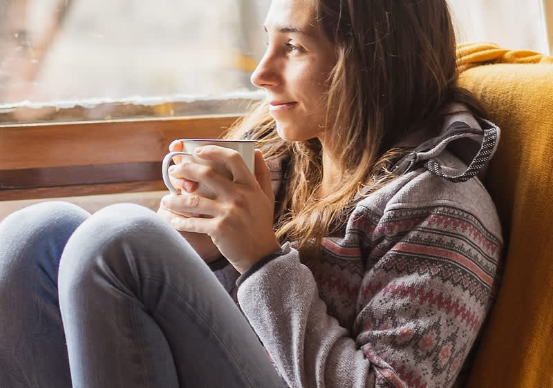 Ženska v puloverju s skodelico ob oknu