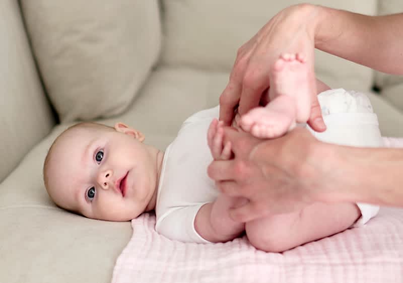 Dojenček na kavču z odraslo osebo, ki drži njegove noge