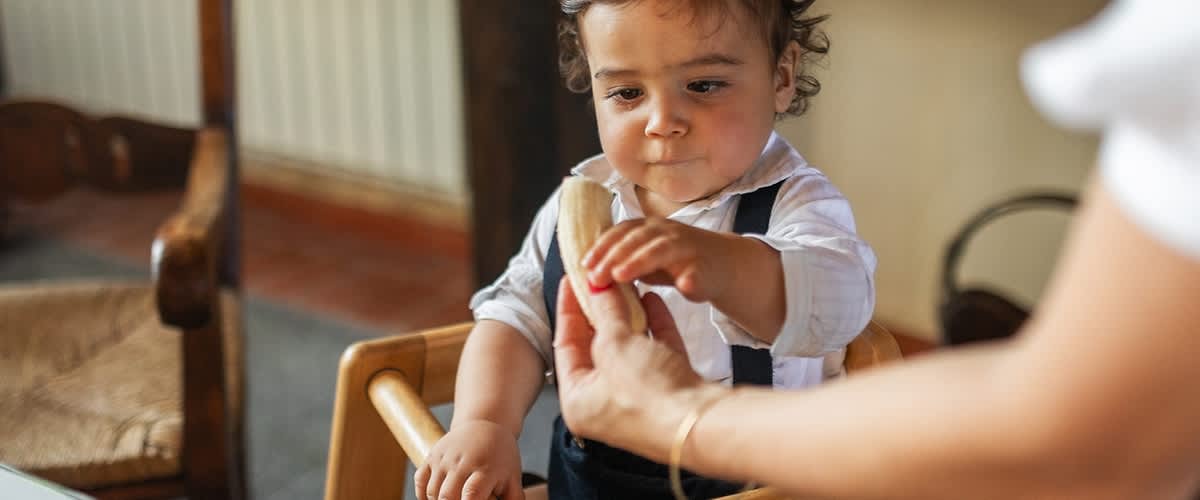 Otrok v stolčku prejema piškot iz roke odrasle osebe