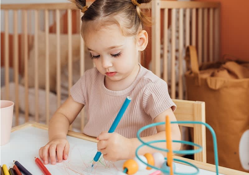 Otrok riše z barvicami za mizo v otroški sobi