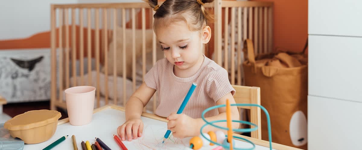 Otrok riše z barvicami za mizo v otroški sobi