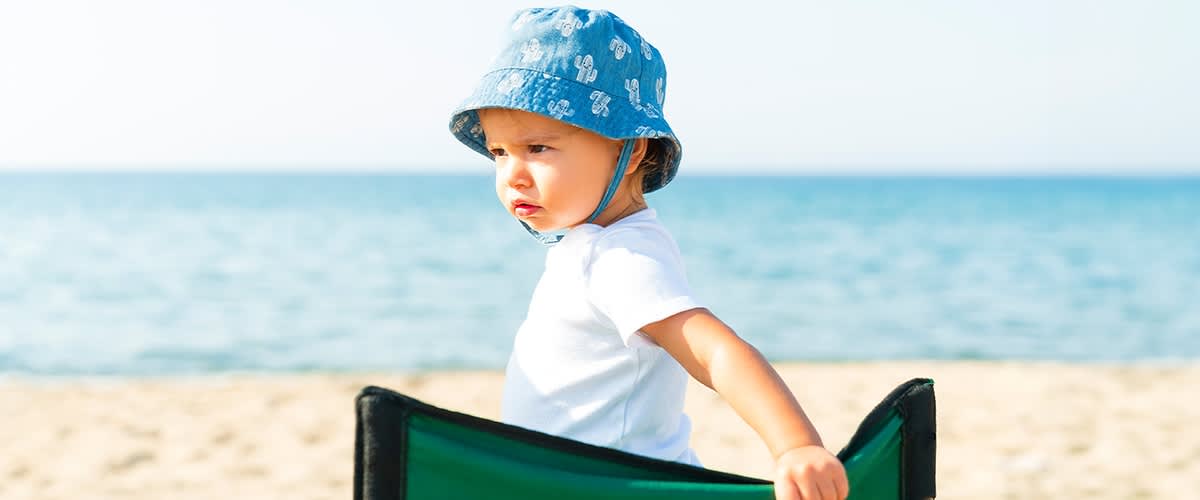 Otrok z modrim klobukom na plaži ob morju