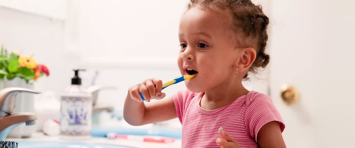 Otrok z roza majico si ščetka zobe v kopalnici