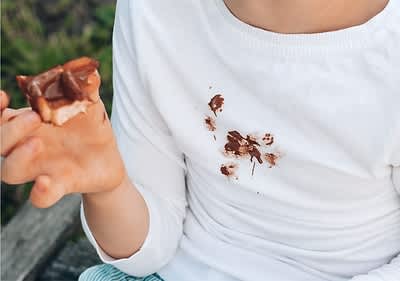 Otrok v beli majici z madežem čokolade na prsih