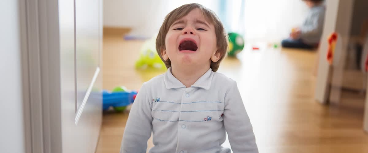 Otrok v belem puloverju sedi na tleh v dnevni sobi z igračami v ozadju