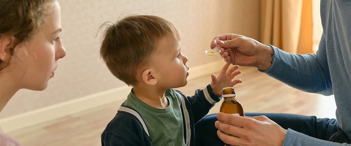 Otrok prejema zdravilo iz stekleničke s kapalko v roki odrasle osebe