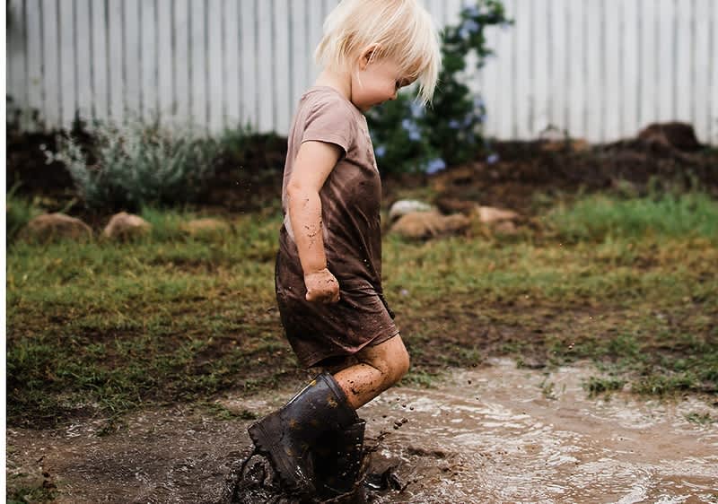 Otrok v blatnih škornjih hodi po blatu na vrtu