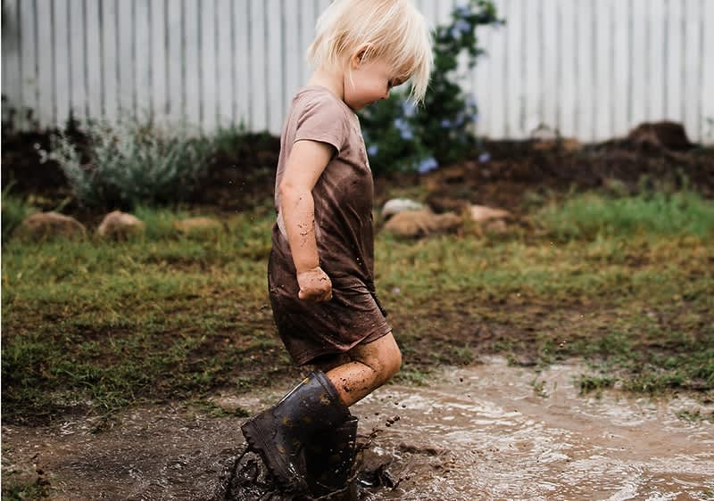 Otrok v blatnih škornjih hodi po blatu na vrtu