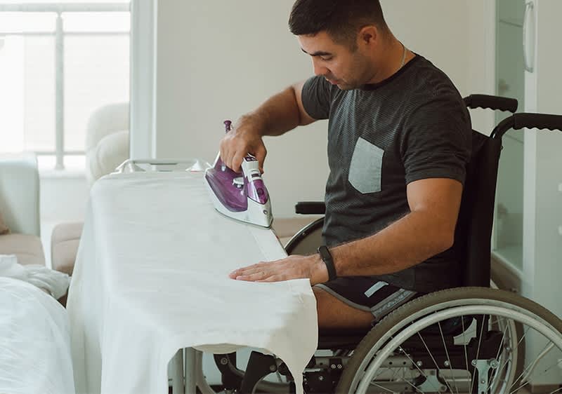 Moški v invalidskem vozičku likalna deska likalnik domače okolje.