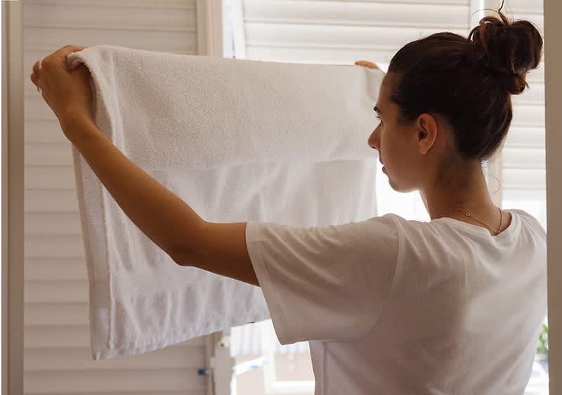Ženska drži bel brisačo pred oknom s senčili.