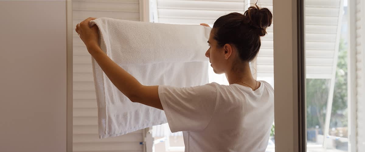 Ženska drži bel brisačo pred oknom s senčili.