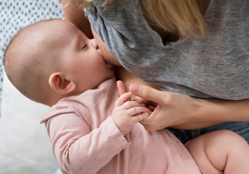 Dojenček v roza oblačilih v naročju mamice v sivem puloverju