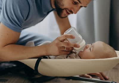 Oče hrani dojenčka s stekleničko v zibelki