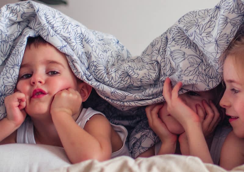 Otroci se igrajo pod odejo s cvetličnim vzorcem