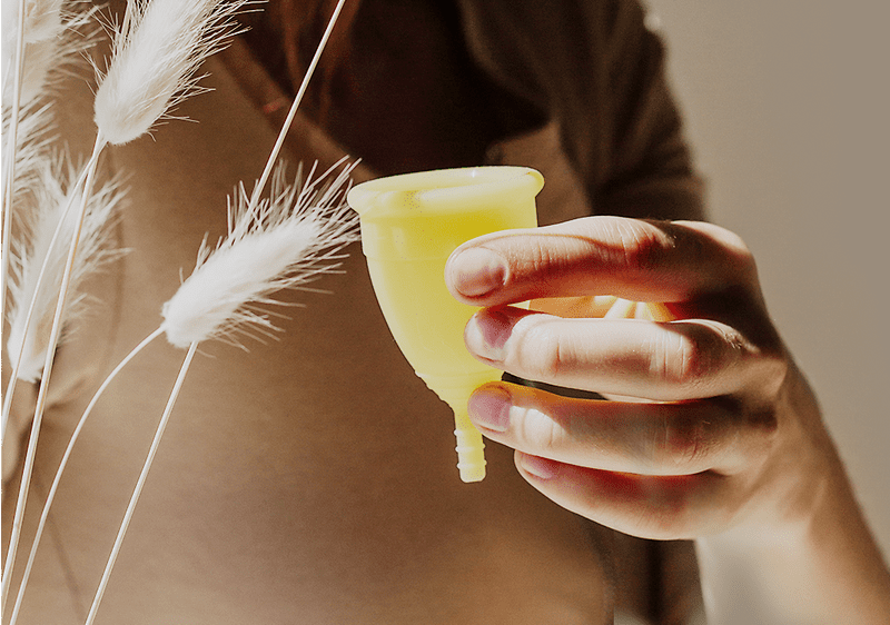 Hand hält gelbe Menstruationstasse