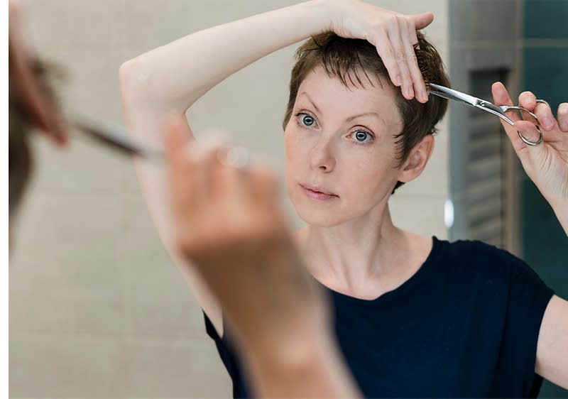 Oseba striže svoje lase s škarjami pred ogledalom