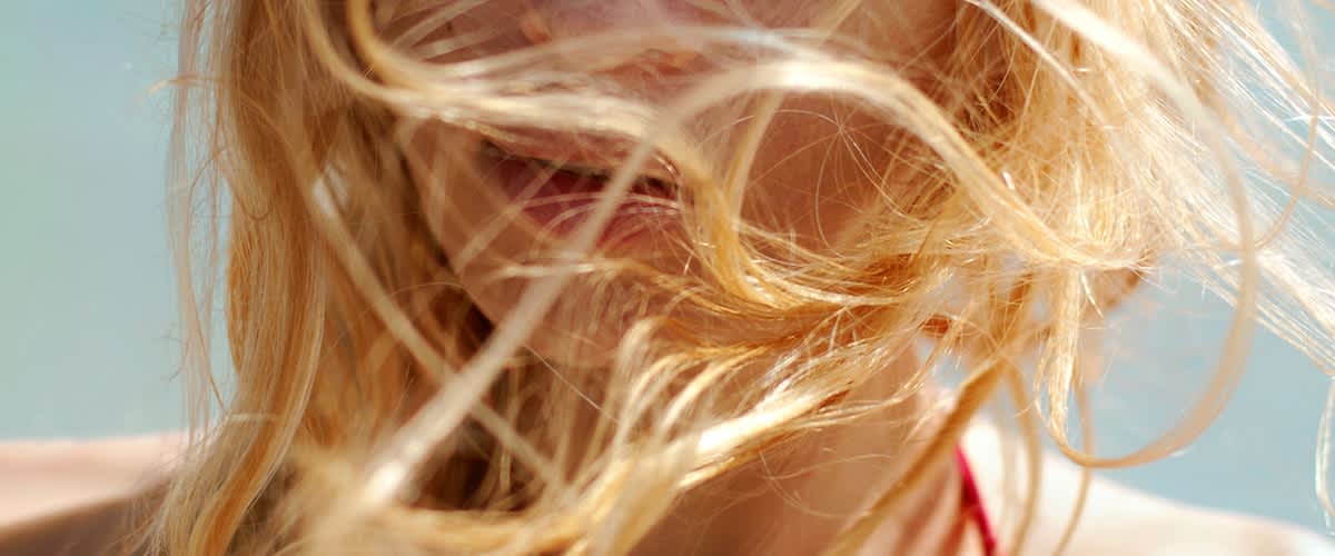 Alt-Text Blond lasje v vetru s svetlimi prameni in modrim ozadjem