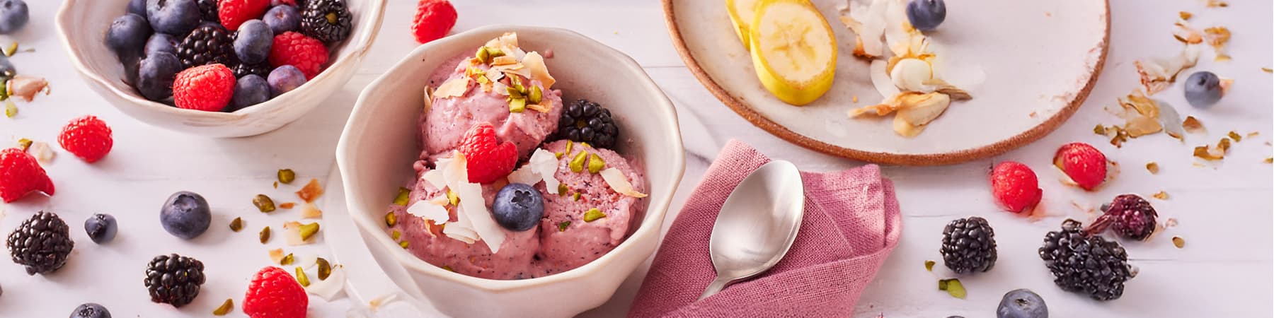 Sladoled z jagodičevjem, kokosom in pistacijami v skledi na mizi.