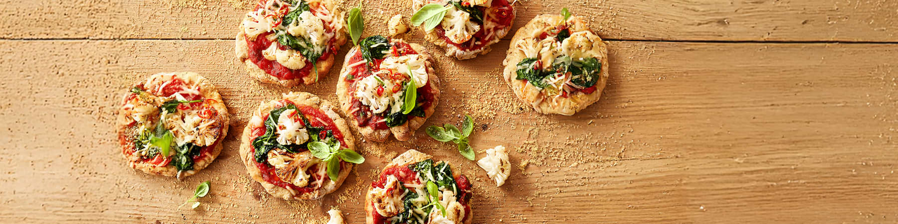 Alt-Text Mini cvetačne pice s paradižnikom in špinačo na leseni površini