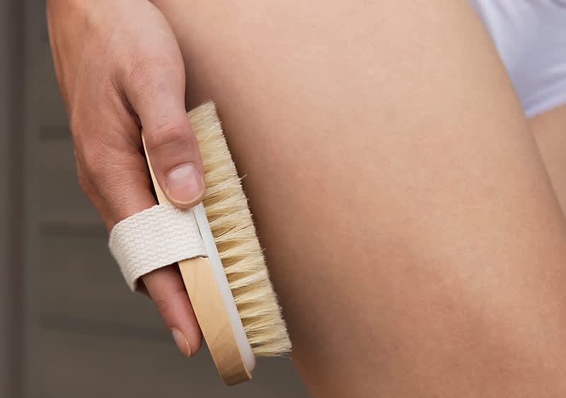 Alt-Text "Suho ščetkanje kože na stegnu z leseno krtačo"