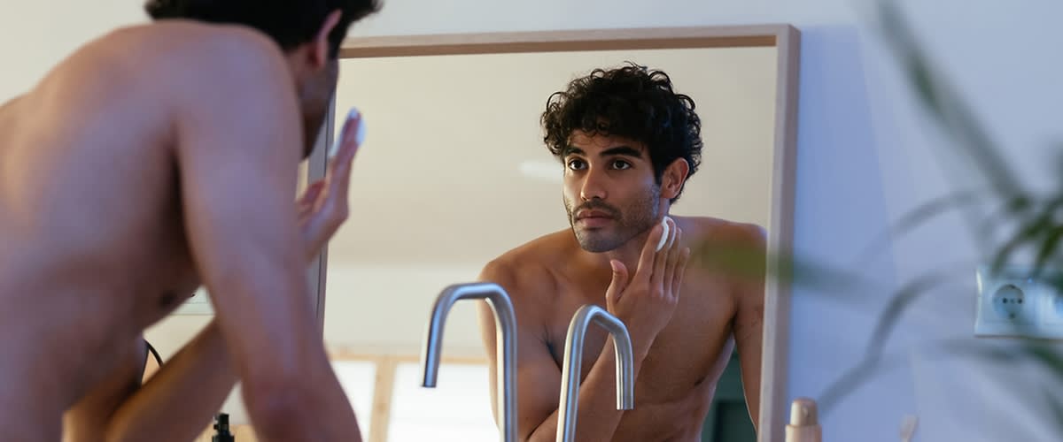 Moški se brije pred ogledalom v kopalnici.