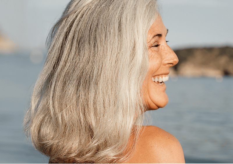 Ženska s sivimi lasmi ob morju in obali v ozadju