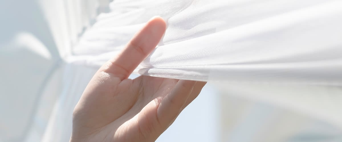 Alt-Text Roka nežno drži belo zaveso v sončni svetlobi