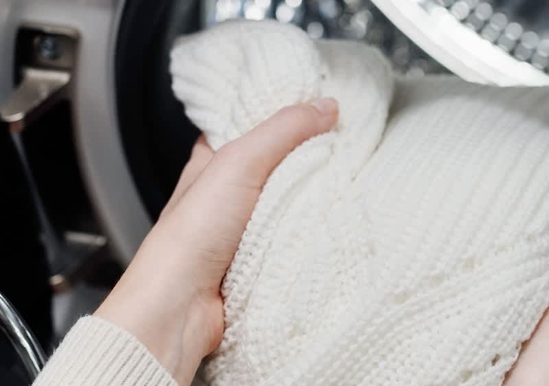 Alt-Text: Oseba drži bel pulover pred pralnim strojem