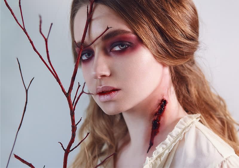 Alt-Text Veje z rdečimi trni ob ženski z rdečimi lasmi in belo obleko