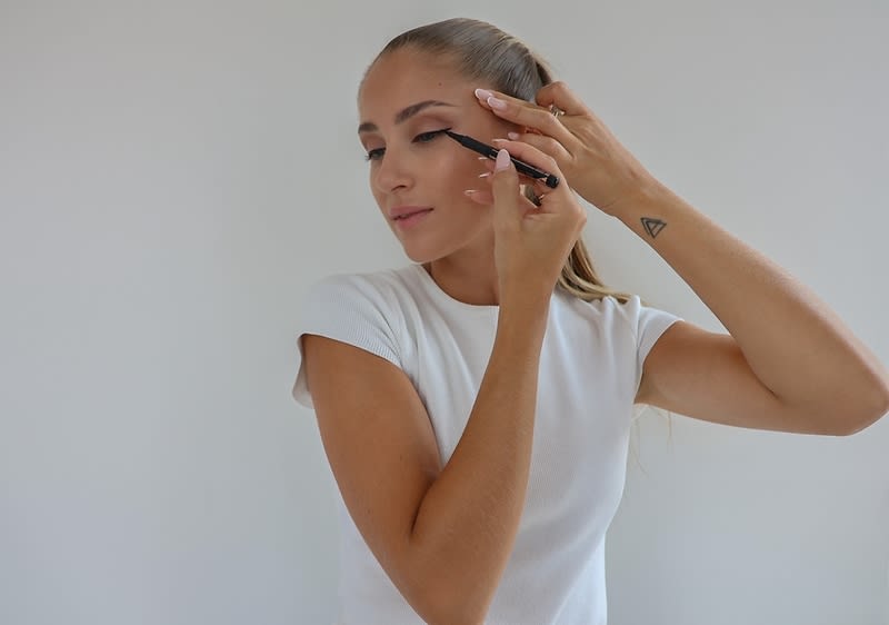 Alt-Text: Ličenje z eyelinerjem na očesu ženske z dolgimi svetlimi lasmi