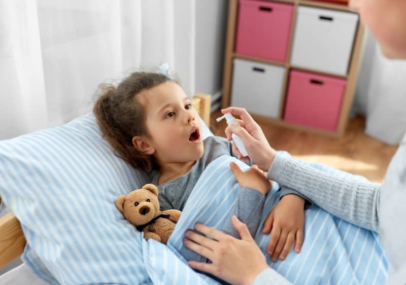 Otrok v postelji z medvedkom, oseba drži pršilo