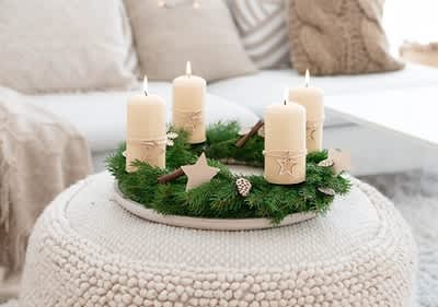 Alt-Text Adventni venec s štirimi svečami na belem pufu v dnevni sobi
