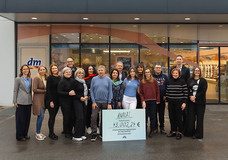 Skupina ljudi pred trgovino dm drži velik ček