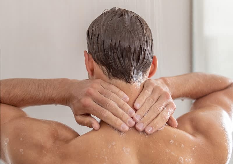 Alt-tekst: Oseba pod prho z mokrimi lasmi in rokami na vratu.