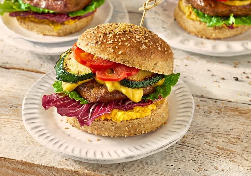 Alt-tekst: Hamburger z zelenjavo, sirom in solato na beli krožniku.