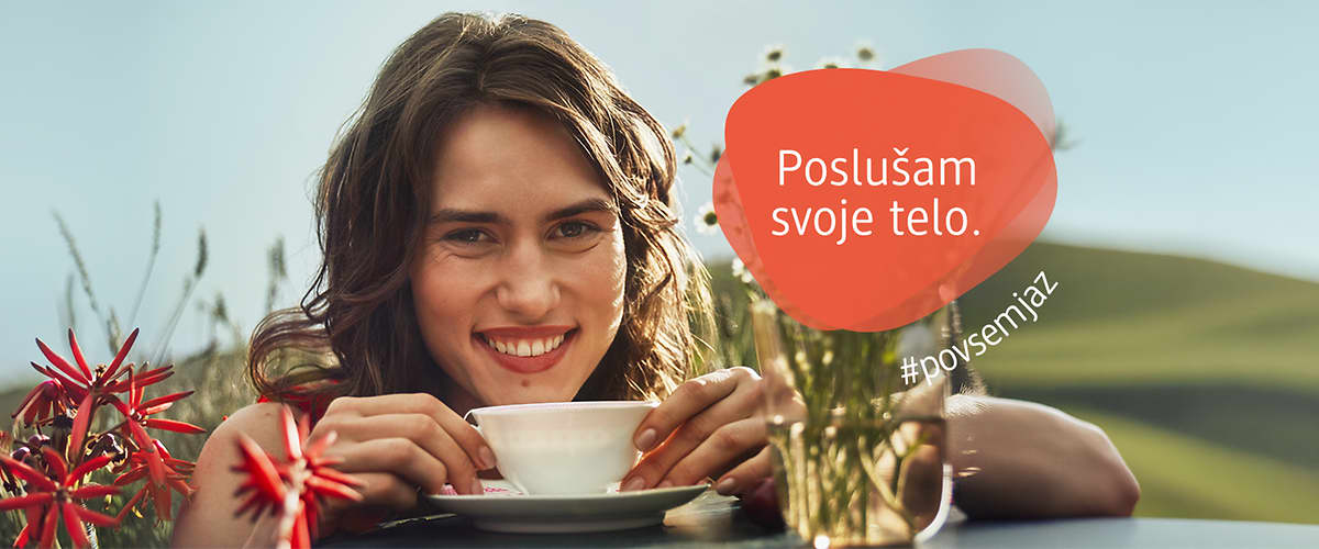 Poslušam svoje telo napis na rdečem oblačku ob skodelici čaja na mizi s cvetjem