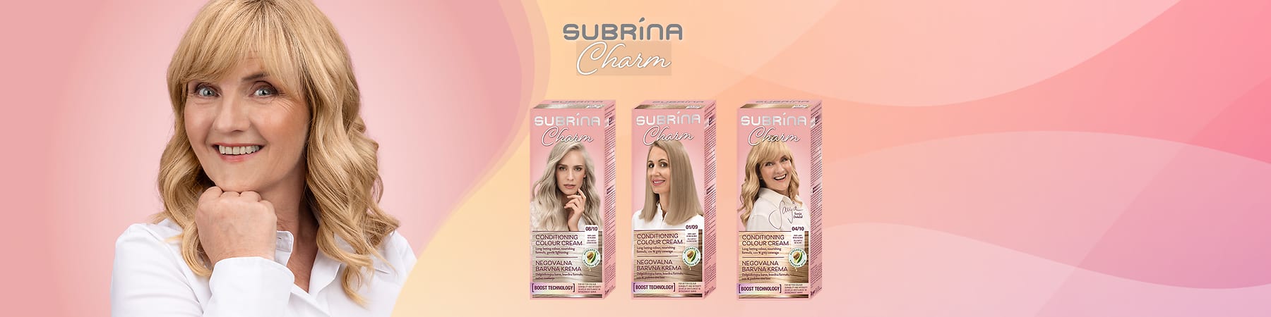 Ženska z blond lasmi nasmejana ob škatlicah barve za lase Subrina Charm, embalaže prikazane spredaj