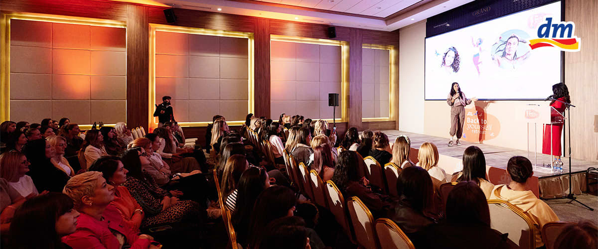 Slika koja prikazuje žensku publiku na konferenciji u sali sa govornicama na pozornici