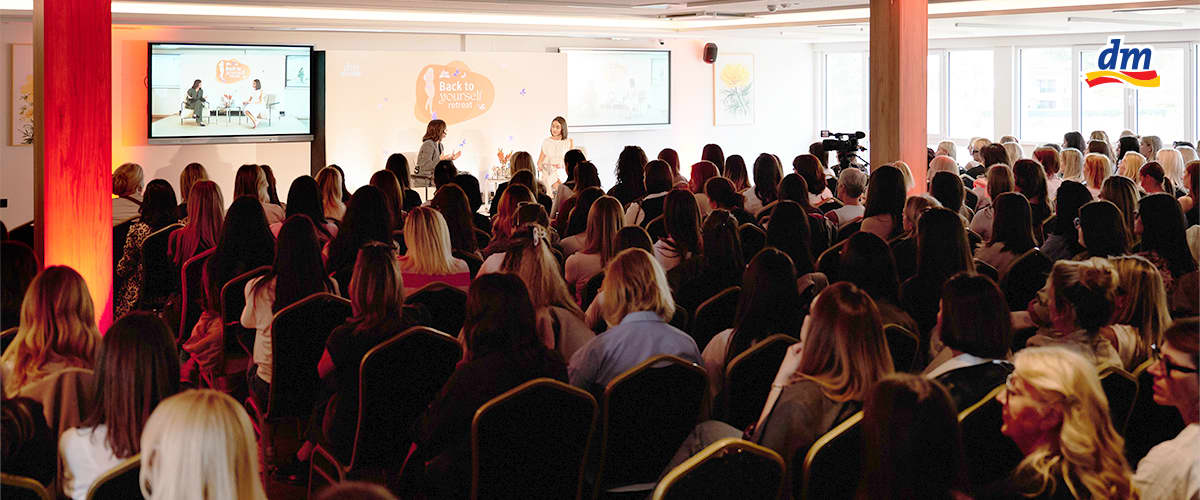 Slika koja prikazuje veliki okupljeni auditorijum na ženskom događaju sa govornicama na bini