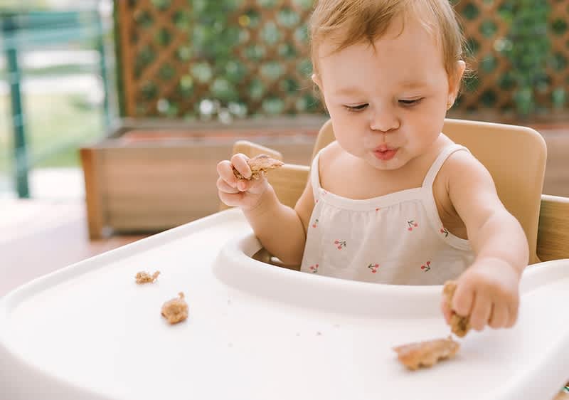 Baby sitzt in Hochstuhl und probiert Essen