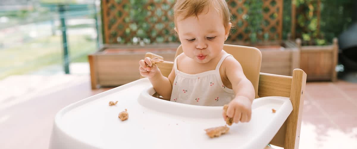 Baby sitzt in Hochstuhl und probiert Essen